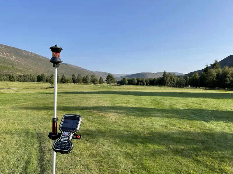 A GNSS survey pole with a controller, in a Highland glen