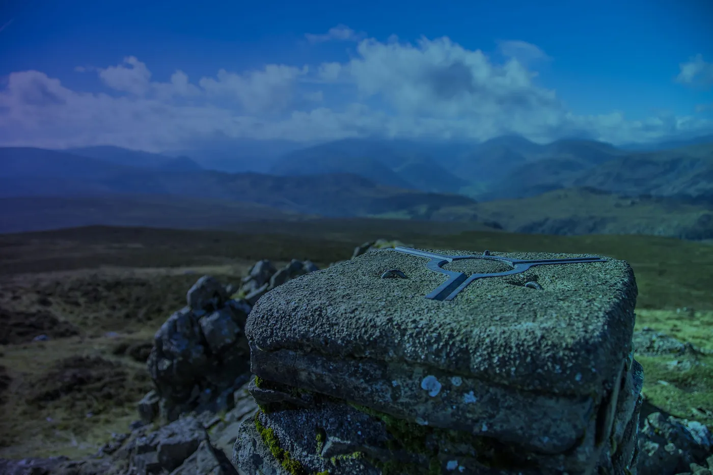 An OS trig pillar on open moorland with the mountains of Scotland behind